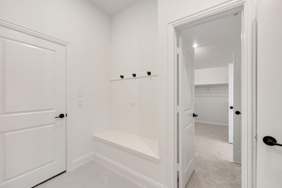 Mudroom with built-in bench, black coat hooks, and doorway leading to a walk-in closet Mudroom with built-in bench, black coat hooks, and doorway leading to a walk-in closet