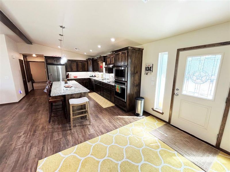 Kitchen featuring dark brown cabinetry, recessed lighting, dark wood-type flooring, a breakfast bar, and appliances with stainless steel finishes Kitchen featuring dark brown cabinetry, recessed lighting, dark wood-type flooring, a breakfast bar, and appliances with stainless steel finishes