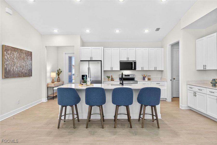 Kitchen featuring a breakfast bar, white cabinetry, light wood-style floors, a kitchen island with sink, and appliances with stainless steel finishes