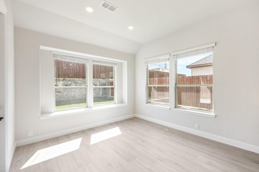 Empty room with light wood floors, white walls, and multiple windows overlooking a fenced backyard