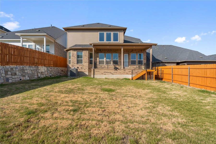 A wooden fence encloses the grassy yard leading up to the covered rear porch.