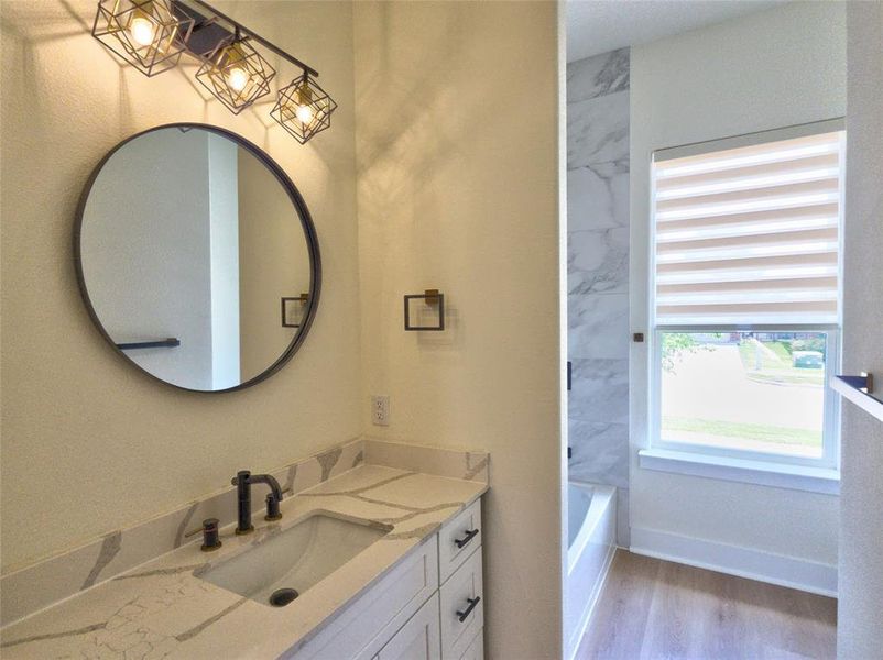 Bathroom vanity featuring a vessel sink with a dark bronze faucet, a round mirror, and an industrial-style light fixture