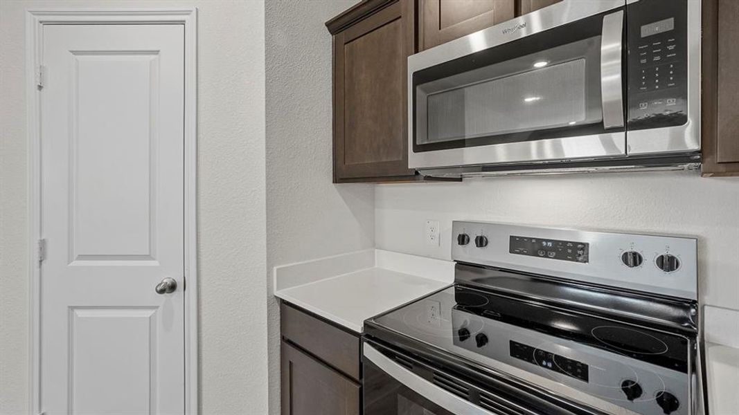 Kitchen featuring stainless steel appliances including an electric range and built-in microwave, white countertops, and dark wood cabinetry