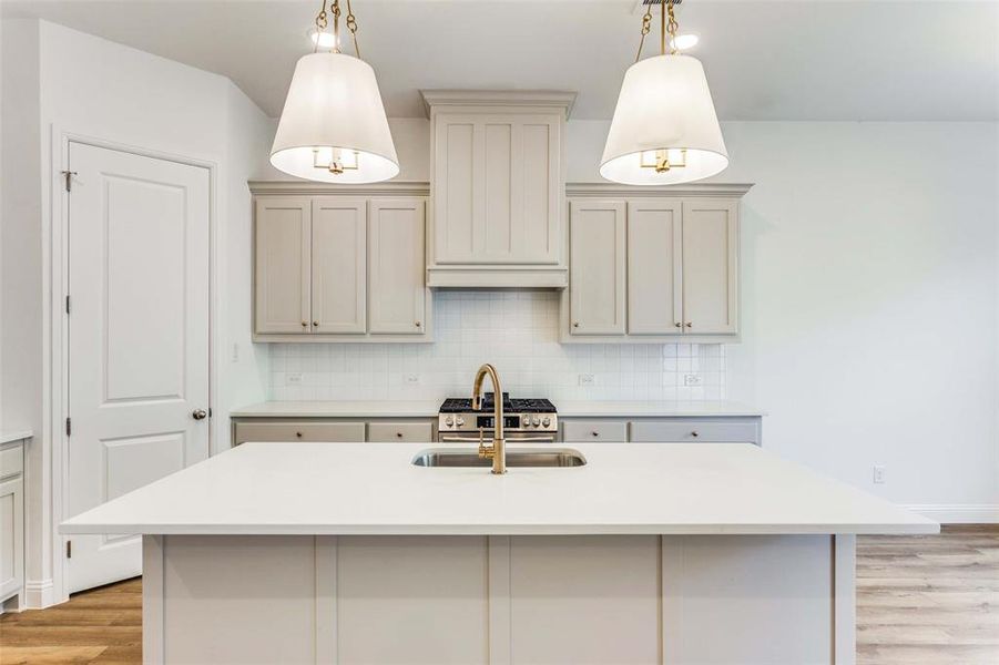 Kitchen featuring pendant lighting, sink, a kitchen island with sink, and tasteful backsplash