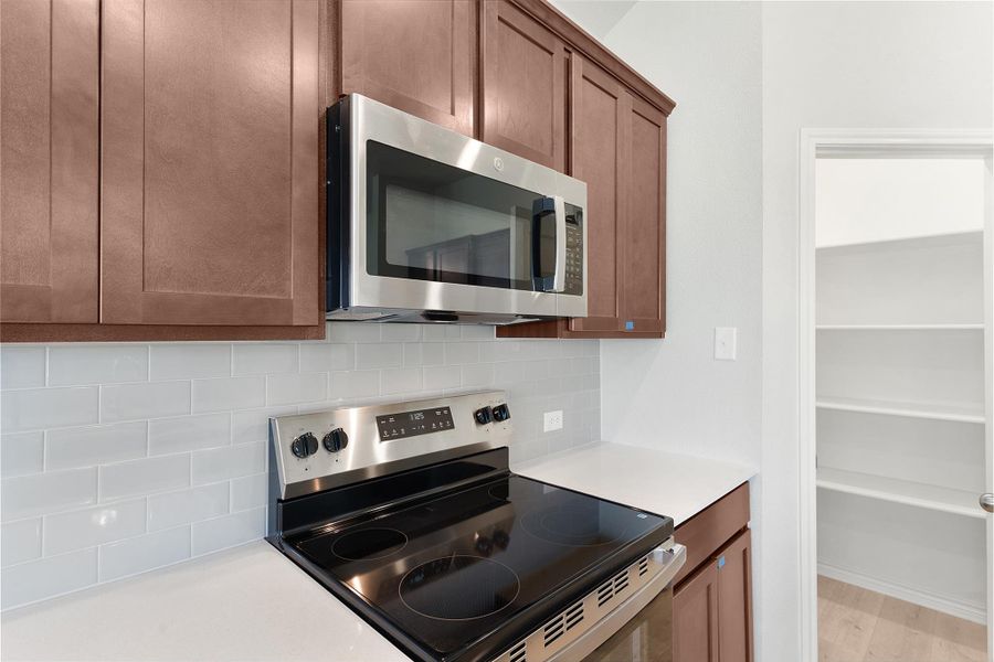 Kitchen featuring stainless steel appliances, light countertops, tasteful backsplash, and wood finished floors Kitchen featuring stainless steel appliances, light countertops, tasteful backsplash, and wood finished floors