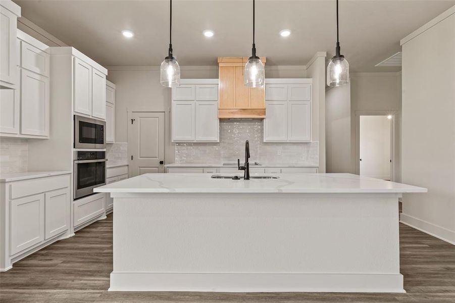 Kitchen island featuring a white countertop with a built-in sink and matte black faucet, complemented by three pendant lights Kitchen island featuring a white countertop with a built-in sink and matte black faucet, complemented by three pendant lights