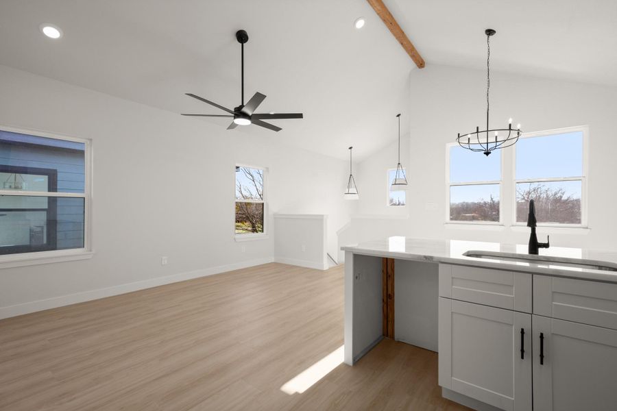 Kitchen with light wood-style floors, open floor plan, hanging lights, ceiling fan, and light stone countertops