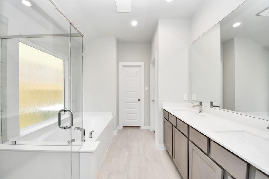 Escape to a spa-like oasis in this primary bathroom. Enjoy a walk-in shower with tile surround, a separate garden tub with custom detailing, and an elegant vanity featuring light countertops, modern hardware, and beautiful recessed lights. Experience luxury and relaxation in every detail. Sample photo of completed home with similar floor plan. Actual colors and selections may vary.