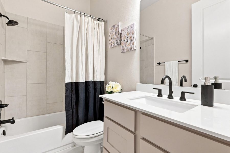 A well-appointed bathroom features a modern vanity with a single sink, elegant dark fixtures, and a clean tub-shower combination.
