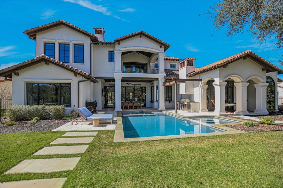 Rear view of house with a balcony, ceiling fan, a chimney, and a yard