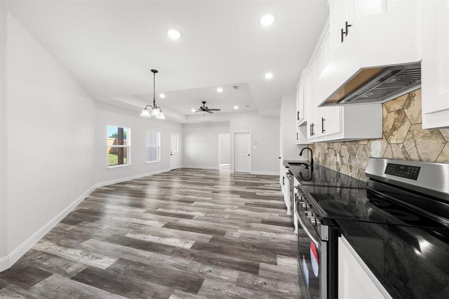 Kitchen featuring stainless steel electric range, a raised ceiling, white cabinets, wood finished floors, and a chandelier Kitchen featuring stainless steel electric range, a raised ceiling, white cabinets, wood finished floors, and a chandelier