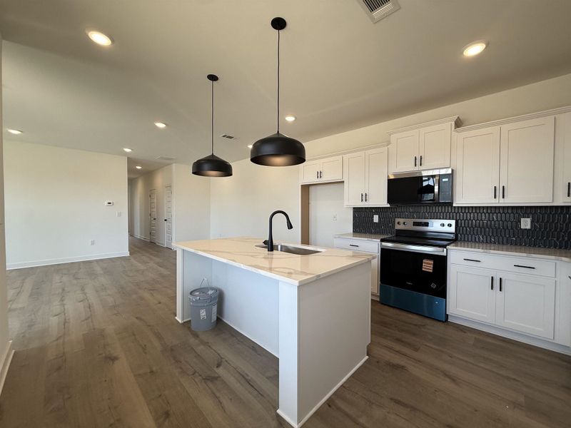 Kitchen featuring stainless steel appliances, white cabinetry, decorative backsplash, a kitchen island with sink, and pendant lighting