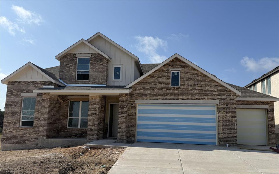 View of front of home with board and batten siding, a garage, driveway, and brick siding View of front of home with board and batten siding, a garage, driveway, and brick siding