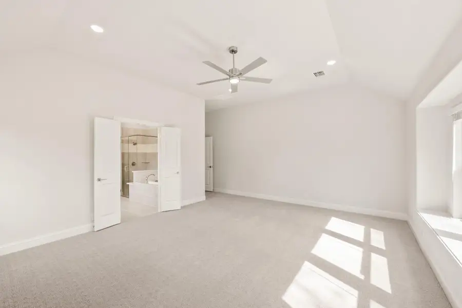 Spacious master bedroom with carpet, ceiling fan, and ensuite bathroom with walk-in shower visible through open doors