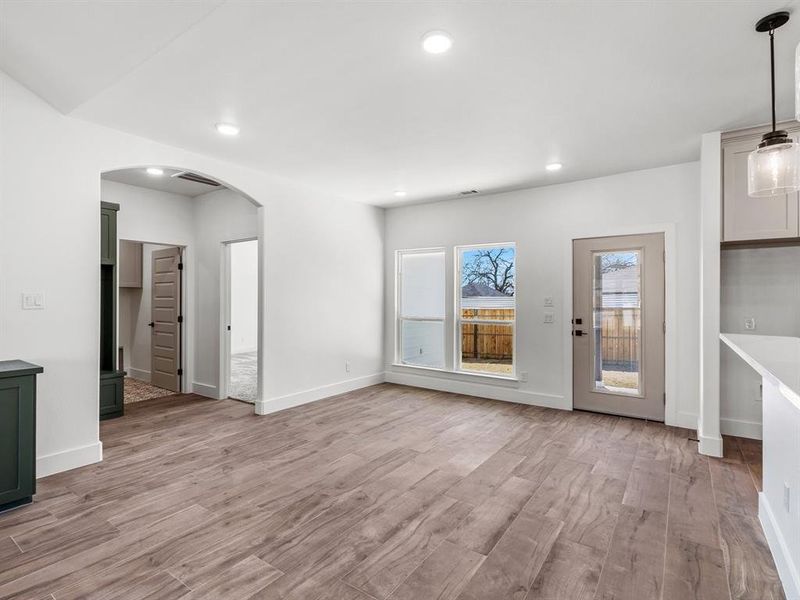 Unfurnished living room featuring light wood-type flooring, visible vents, recessed lighting, arched walkways, and baseboards