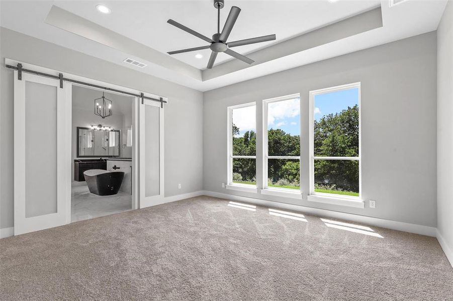 Unfurnished living room with ceiling fan, a barn door, carpet, and a tray ceiling