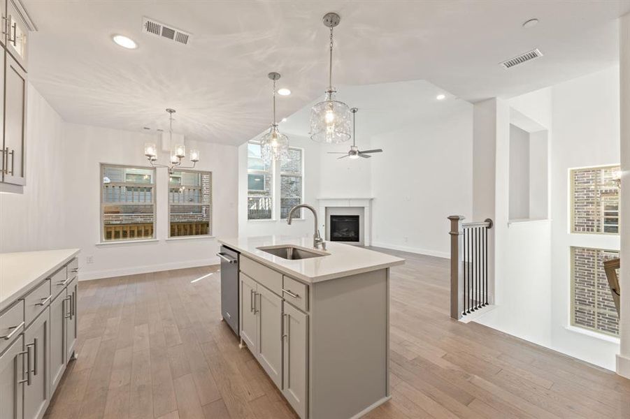 Kitchen with a kitchen island with sink, light hardwood / wood-style flooring, sink, gray cabinets, and decorative light fixtures