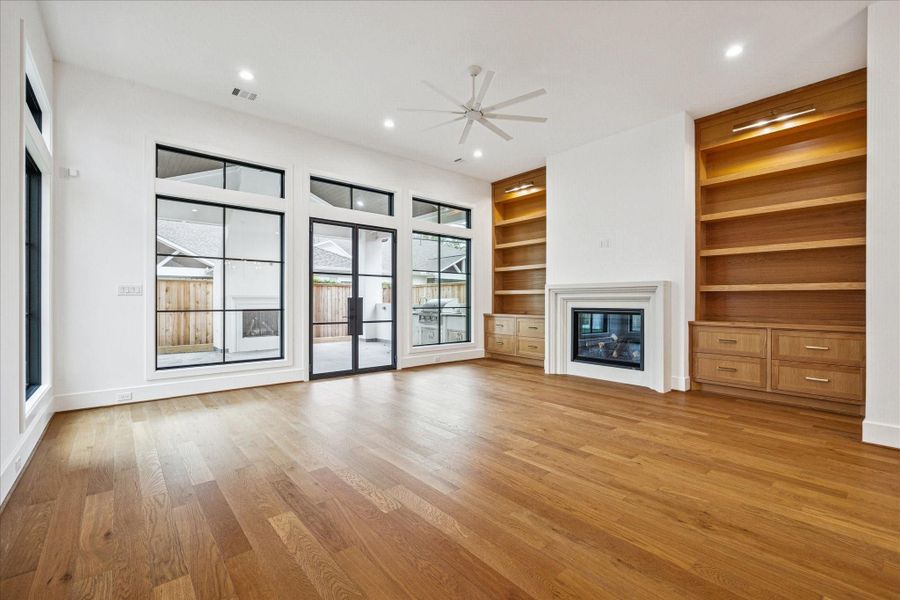 Floor to ceiling windows draw in natural light and frame views of the covered patio and outdoor fireplace. Custom oak built-ins flank a sleek gas fireplace, adding warmth and balance to the room. Floor to ceiling windows draw in natural light and frame views of the covered patio and outdoor fireplace. Custom oak built-ins flank a sleek gas fireplace, adding warmth and balance to the room.
