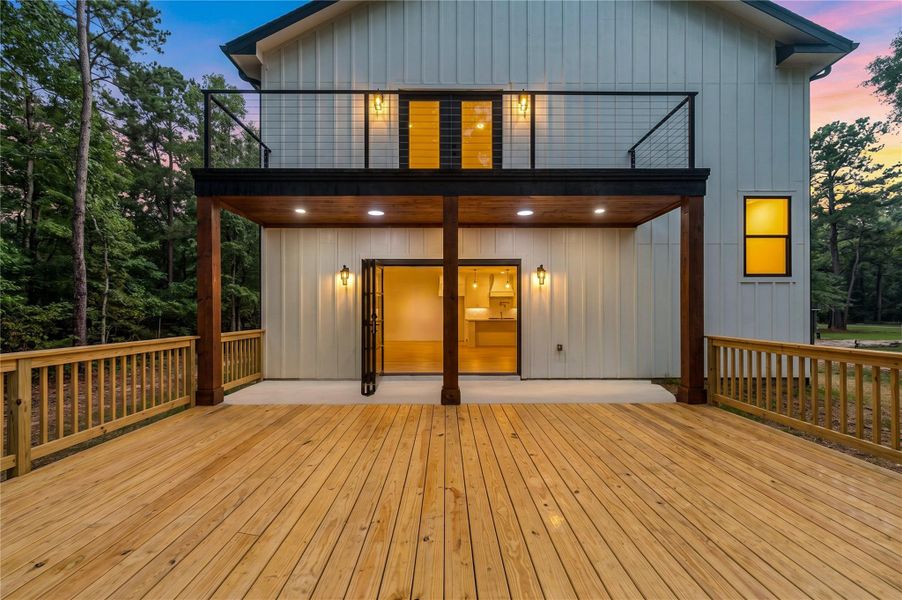 Spacious two-story deck with elegant wood flooring and modern railing, offering seamless indoor-outdoor living surrounded by serene woodland views.