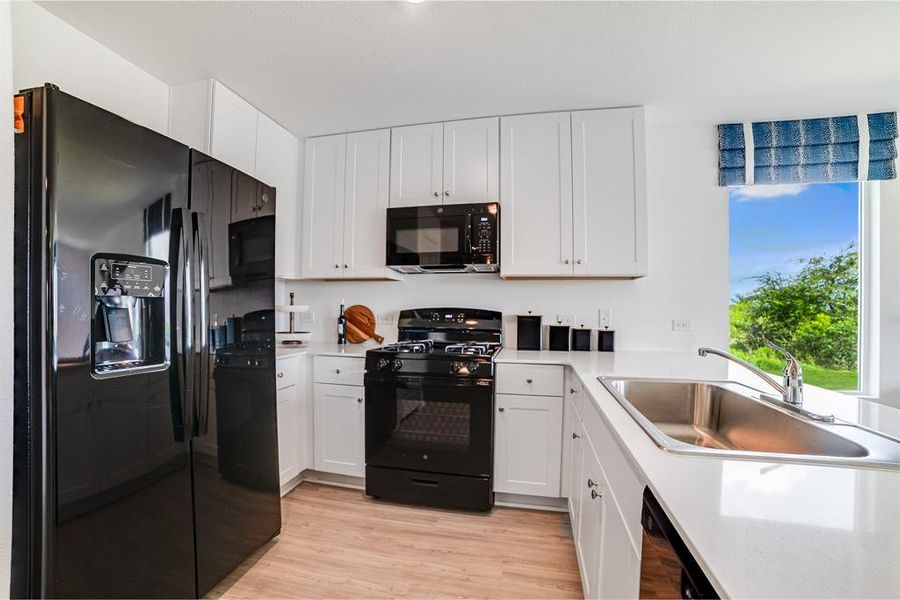 Kitchen with black appliances, white cabinetry, light wood-style floors, and light stone counters Kitchen with black appliances, white cabinetry, light wood-style floors, and light stone counters