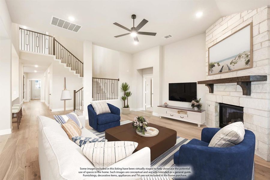 Open living room with stone fireplace, high ceilings, ceiling fan, and staircase with wood floors