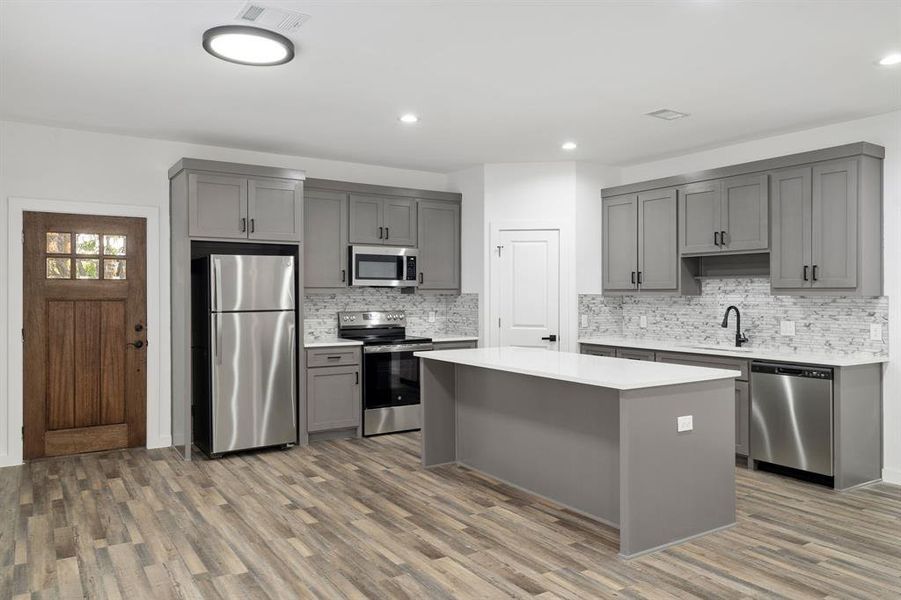 Kitchen with gray cabinets, appliances with stainless steel finishes, and hardwood / wood-style flooring