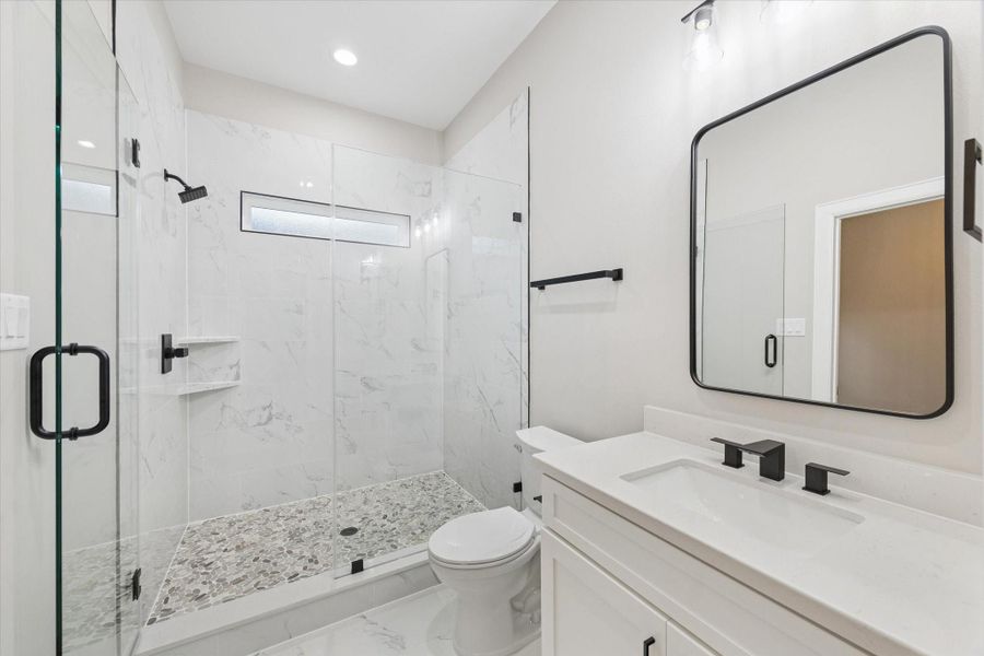 Fourth bedroom ensuite full bath.  Stone-look flooring and frameless shower.  Narrow window for natural light, framed mirror and quartz counter.