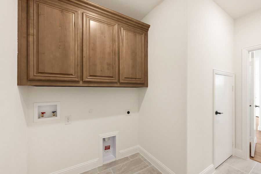 Laundry room with wood upper cabinets, washer hookups, dryer outlet, and tile floor Laundry room with wood upper cabinets, washer hookups, dryer outlet, and tile floor