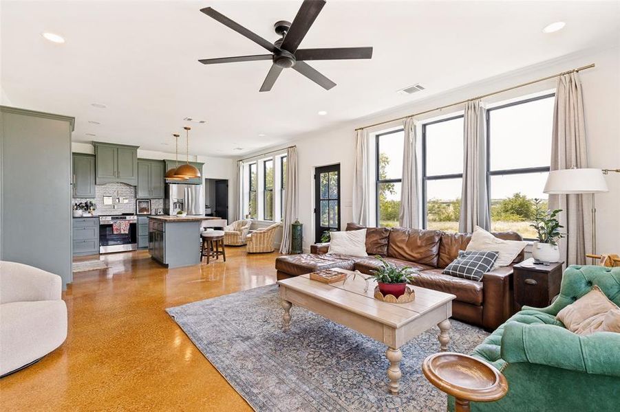 Open-concept living area with a dark-bladed ceiling fan and polished concrete flooring Open-concept living area with a dark-bladed ceiling fan and polished concrete flooring