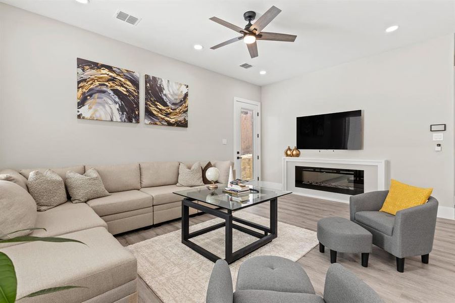 Living room featuring a glass covered fireplace, wood finished floors, recessed lighting, and ceiling fan