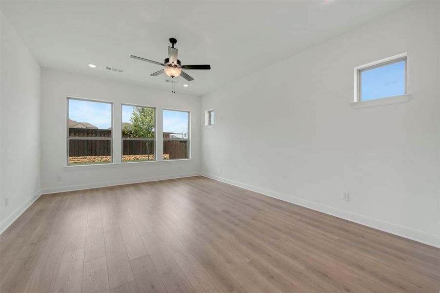 Spacious room featuring wood-finish flooring, white walls, and a contemporary ceiling fan with integrated lighting Spacious room featuring wood-finish flooring, white walls, and a contemporary ceiling fan with integrated lighting