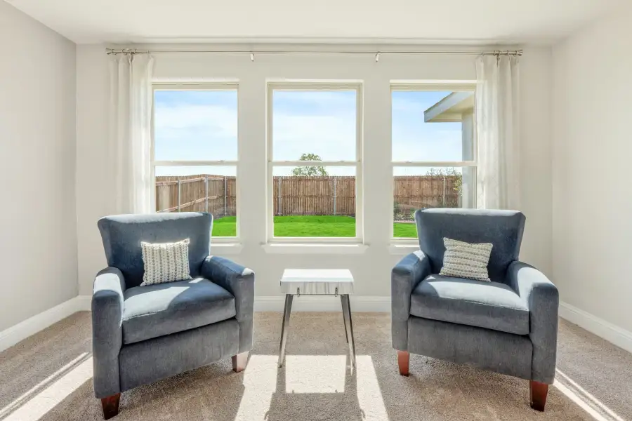 Sitting area with two blue armchairs, small side table, and three windows overlooking a fenced backyard