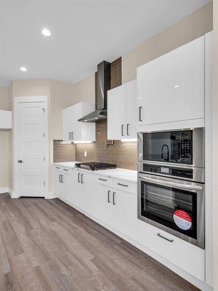 Kitchen featuring appliances with stainless steel finishes, white cabinets, wall chimney range hood, and light wood-type flooring