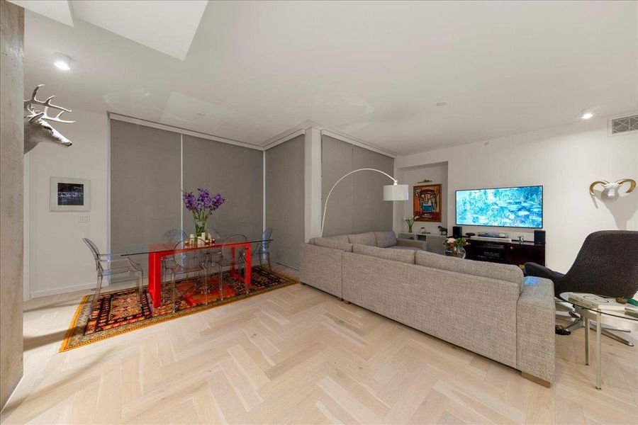 A cohesive living and dining space defined by upgraded herringbone wood floors and custom wired motorized blackout shades, offering privacy and effortless light control. The open layout creates a warm, modern environment ideal for everyday living, film nights, or hosting intimate Omakase-style dinners.