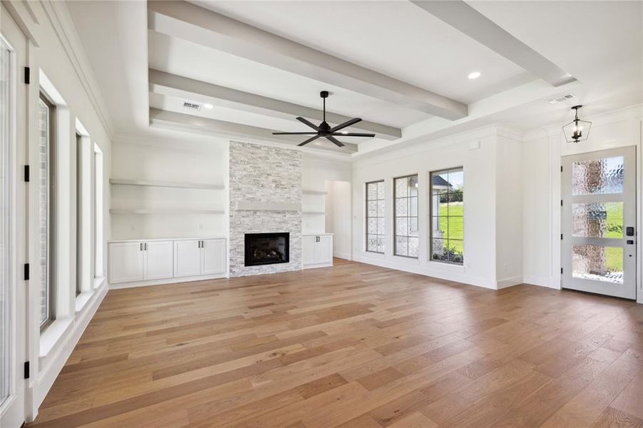 Unfurnished living room with beam ceiling, light hardwood / wood-style flooring, crown molding, a fireplace, and ceiling fan with notable chandelier