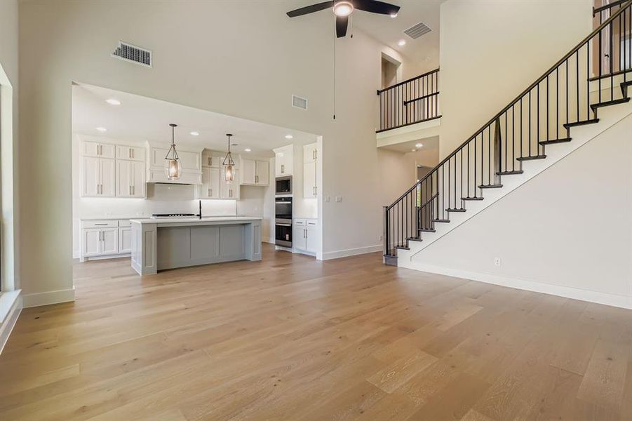 Unfurnished living room with light wood-style flooring, stairs, a ceiling fan, a towering ceiling, and recessed lighting