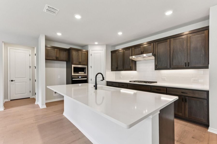 Kitchen featuring tasteful backsplash, recessed lighting, light wood-type flooring, dark brown cabinets, and appliances with stainless steel finishes