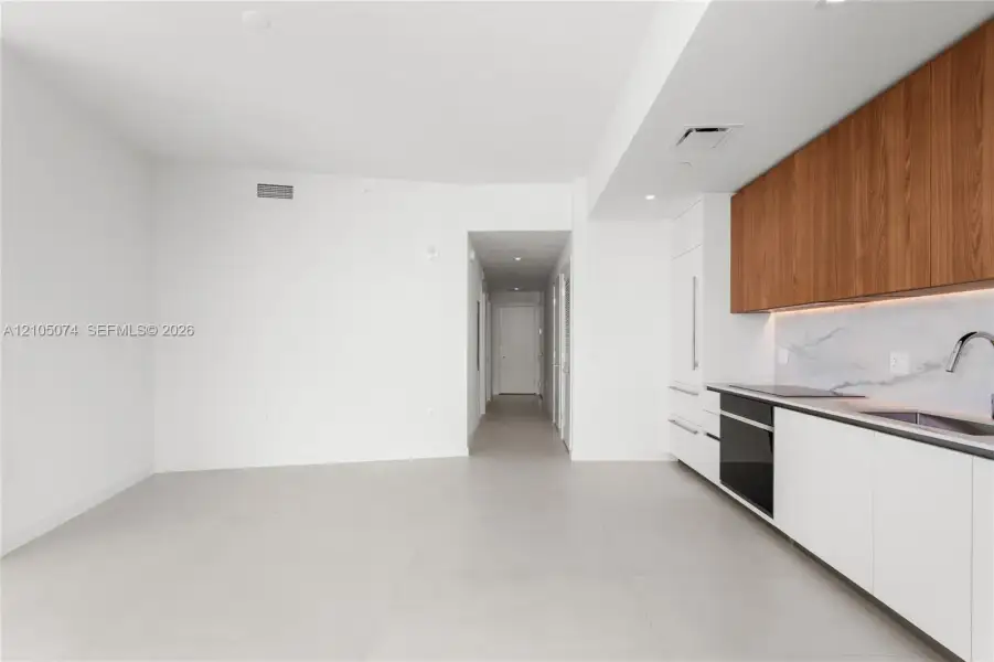 Kitchen featuring wood-finish upper cabinetry, flat-panel white lower cabinetry, stone-surface backsplash, integrated built-in appliances, and large-format tile flooring