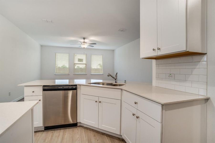 Kitchen with dishwasher, white cabinets, light wood-type flooring, backsplash, and a peninsula