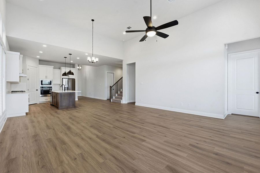 Unfurnished living room with a high ceiling, suspended lighting, dark wood-style floors, and a ceiling fan