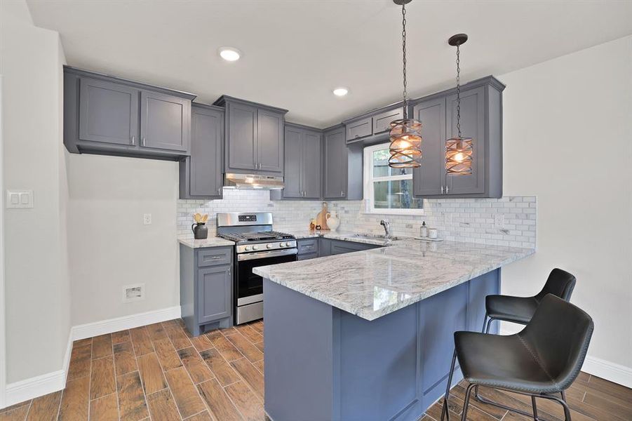 Kitchen with gray cabinetry, sink, gas stove, hanging light fixtures, and dark hardwood / wood-style floors