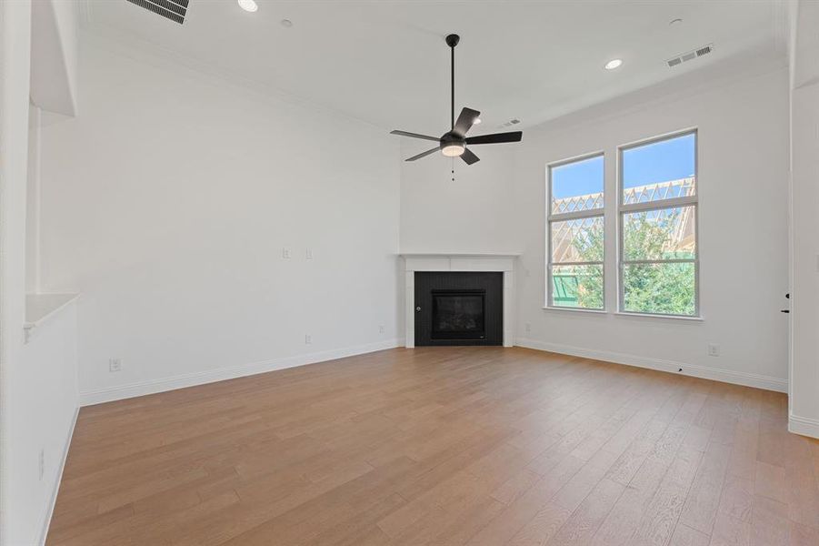 Unfurnished living room with light wood-style floors, ornamental molding, a glass covered fireplace, recessed lighting, and ceiling fan Unfurnished living room with light wood-style floors, ornamental molding, a glass covered fireplace, recessed lighting, and ceiling fan