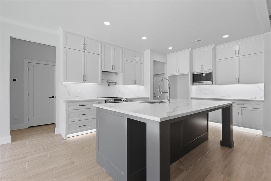 Kitchen with tasteful backsplash, white cabinetry, recessed lighting, light stone countertops, and wood finish floors Kitchen with tasteful backsplash, white cabinetry, recessed lighting, light stone countertops, and wood finish floors