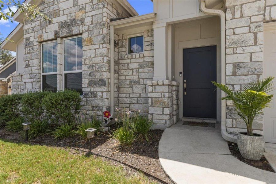 A stone masonry exterior accents the concrete walkway leading to the recessed front entry.