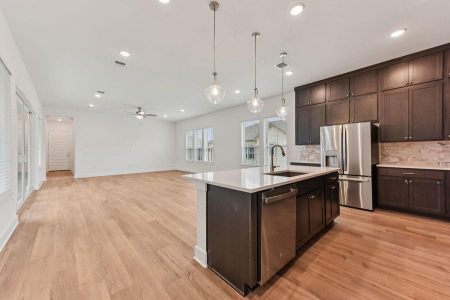 Open-concept living space featuring wood-finish flooring, recessed lighting, and a contemporary kitchen island with a built-in sink