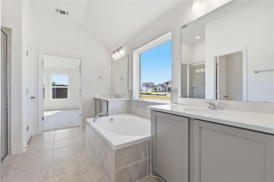 Spacious bathroom featuring a built-in soaking tub, dual vanities with quartz countertops, a separate glass-enclosed shower, and tile flooring
