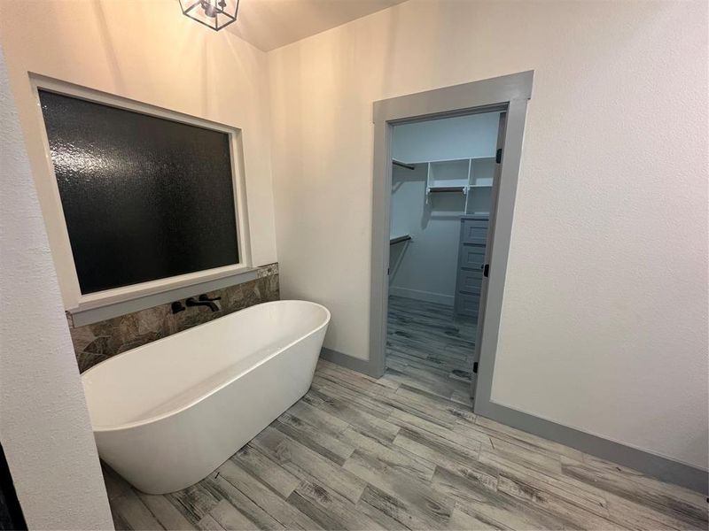 Bathroom with a spacious closet, a soaking tub, and light wood-type flooring