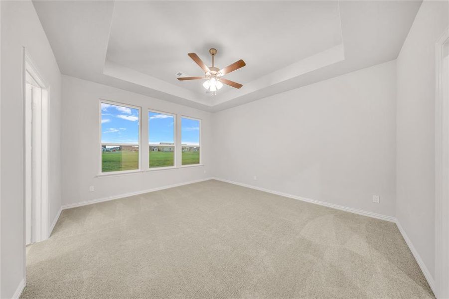 Carpeted empty room with a tray ceiling and ceiling fan Carpeted empty room with a tray ceiling and ceiling fan
