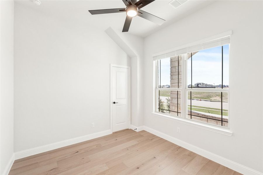 Empty bedroom with vaulted ceiling, ceiling fan, hardwood floors, and large window with neighborhood view