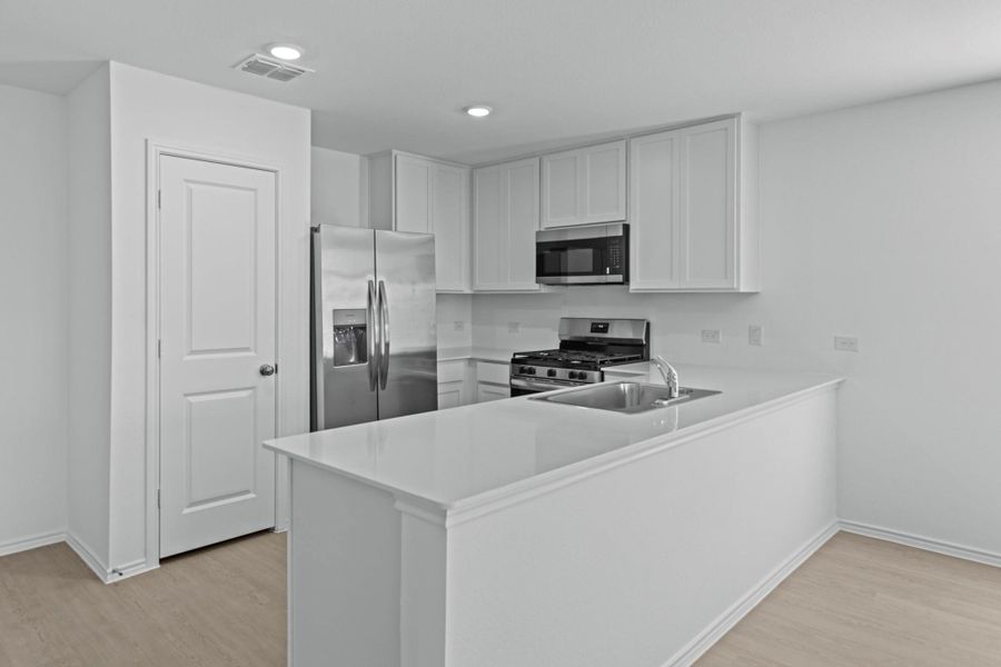 Kitchen with appliances with stainless steel finishes, light countertops, a peninsula, light wood-type flooring, and white cabinets Kitchen with appliances with stainless steel finishes, light countertops, a peninsula, light wood-type flooring, and white cabinets